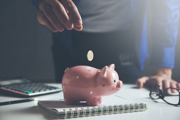 Man putting money in piggy bank on table