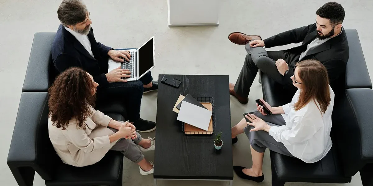four business people sitting on couches in front of a coffee table talking four business people sitting on couches in front of a coffee table talking