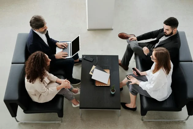 four business people sitting on couches in front of a coffee table talking four business people sitting on couches in front of a coffee table talking