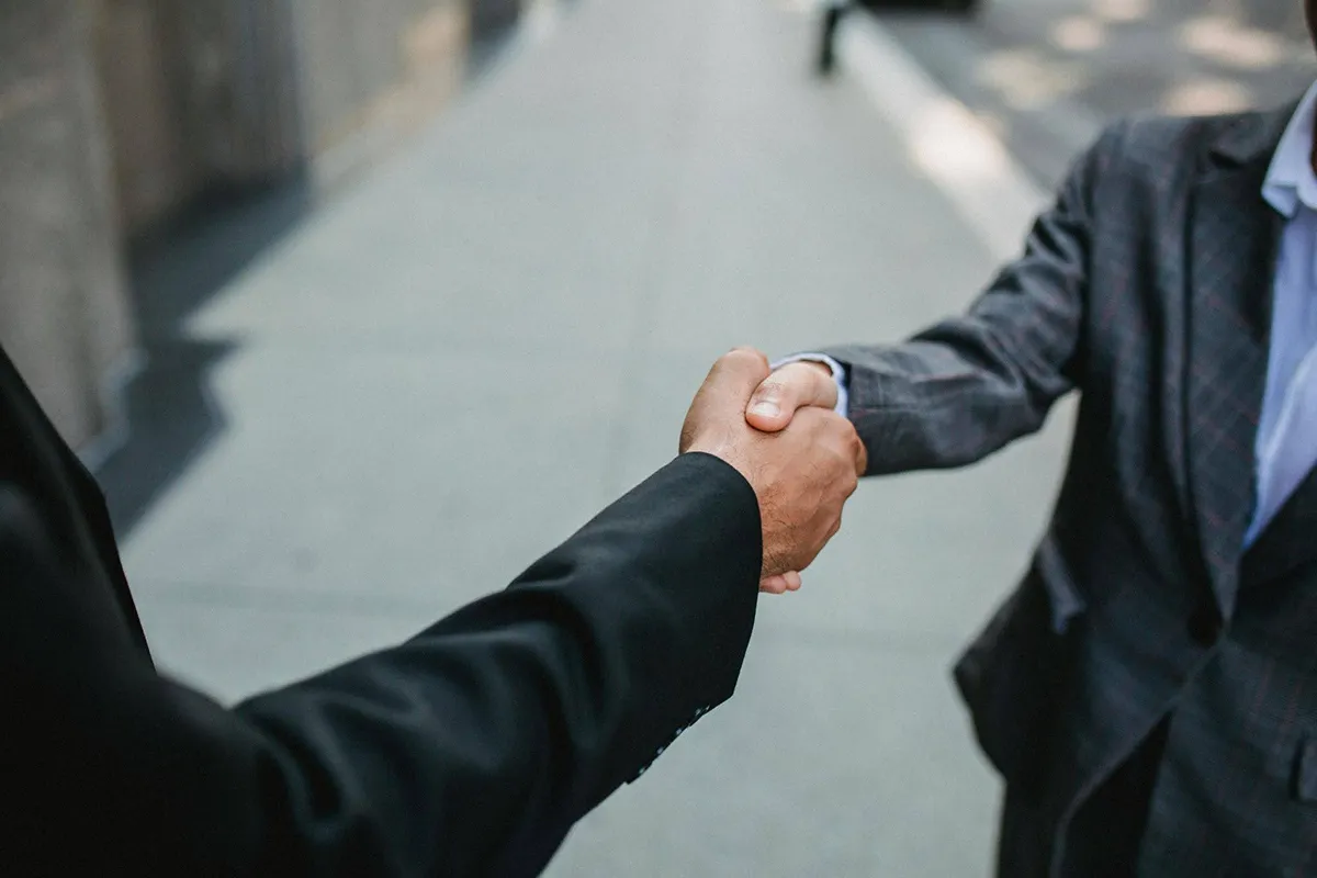 Close-up of two businessmen shaking hands outside, symbolising partnership and agreement Close-up of two businessmen shaking hands outside, symbolising partnership and agreement