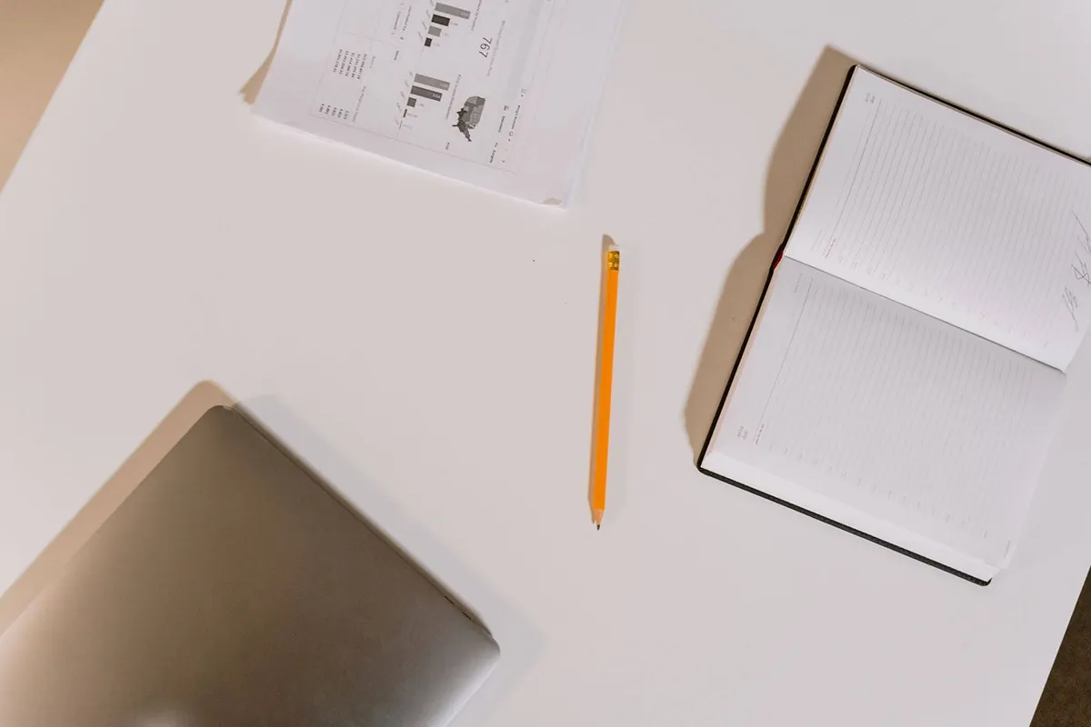 table layout with paper, notebook, laptop, and pencil on a white desk table layout with paper, notebook, laptop, and pencil on a white desk
