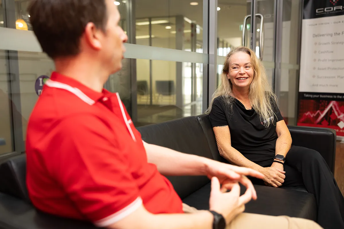 man and lady talk and smiling on an office couch Man and woman sitting on a couch smiling and talking in an office